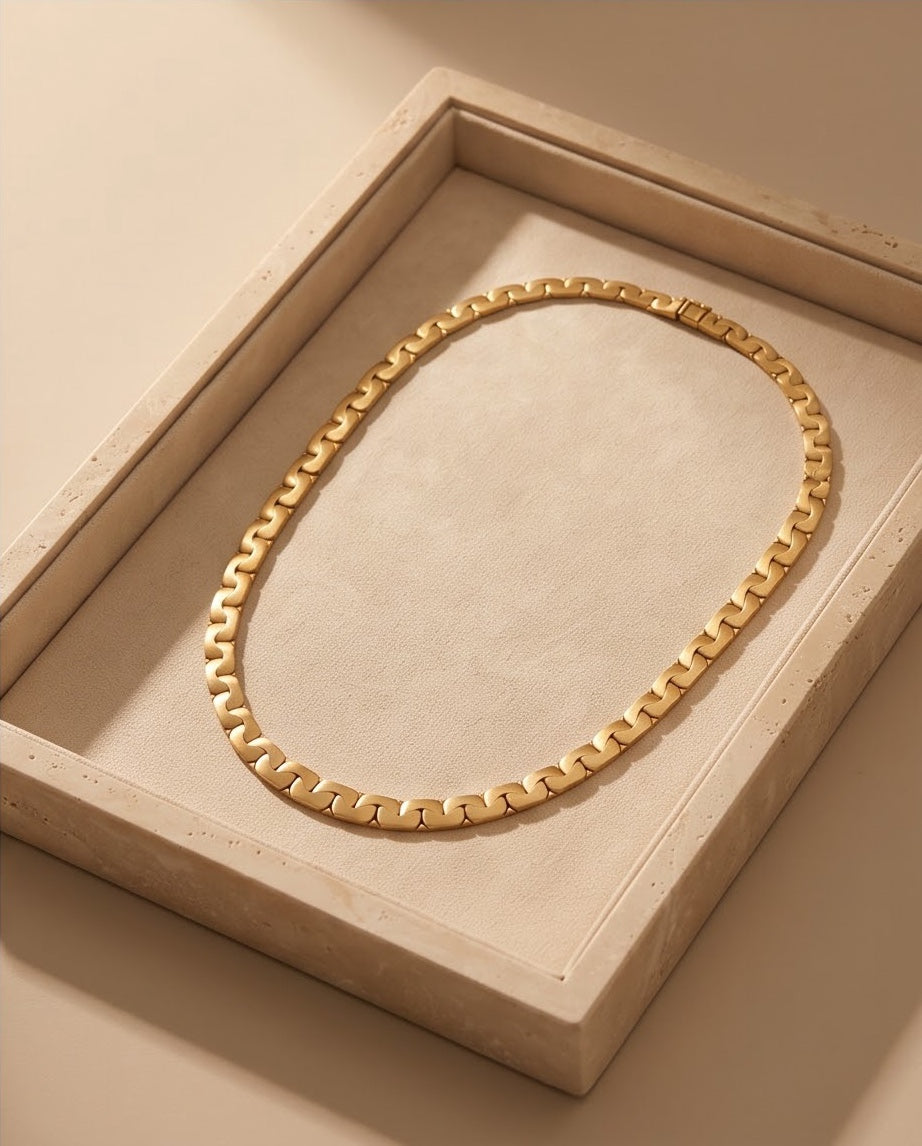 18K gold link collar necklace displayed in a travertine stone jewelry tray