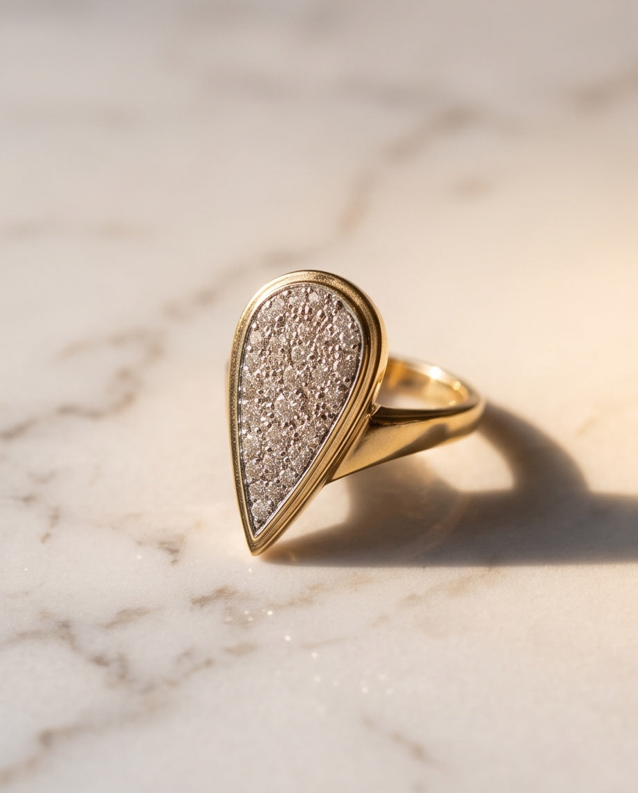 Angled view of the pavé diamond pear-shape plaque ring on marble