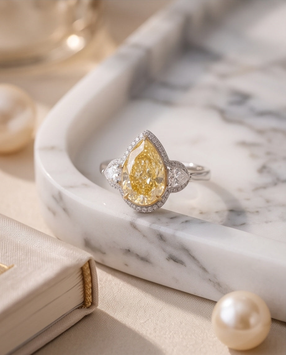 Fancy yellow pear diamond ring on a marble tray with pearls
