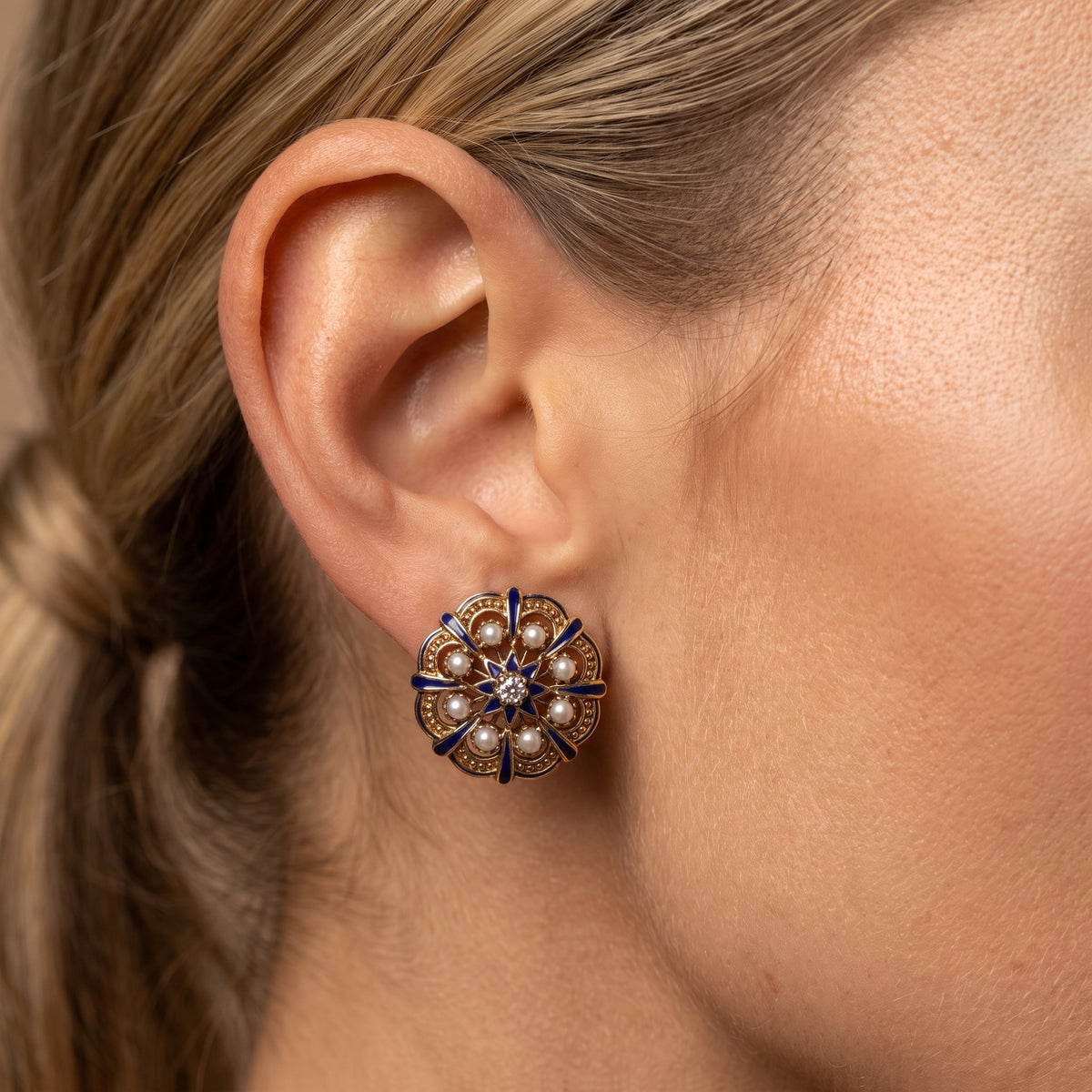 Close-up of blue enamel and seed pearl earring worn on the ear