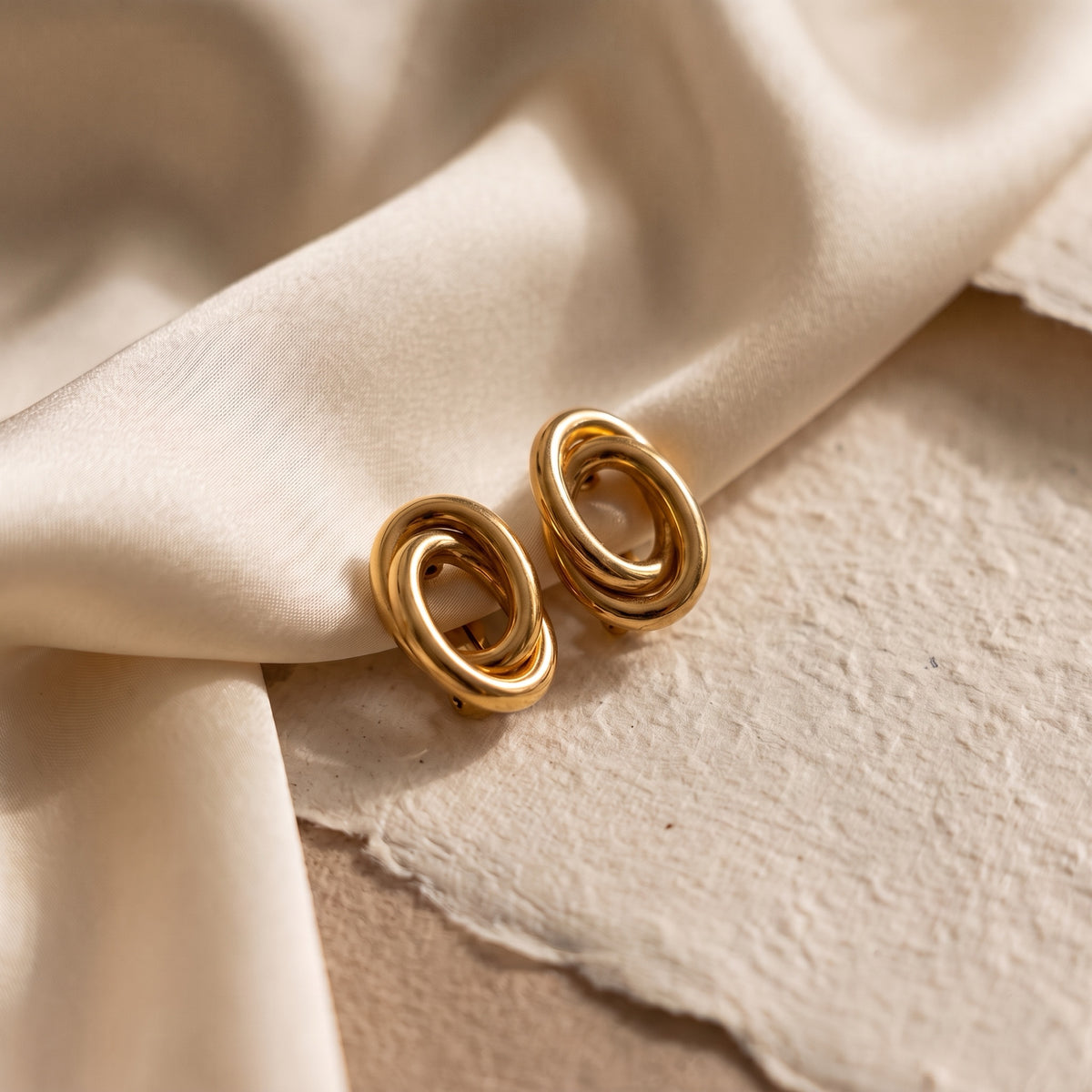 18kt yellow gold interlocking swirl hoop earrings on silk fabric