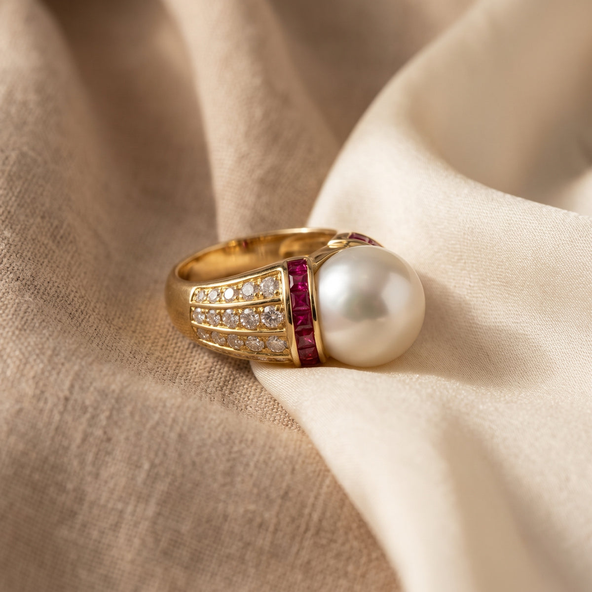 South Sea pearl and ruby dome ring photographed on silk, showing diamond shoulders