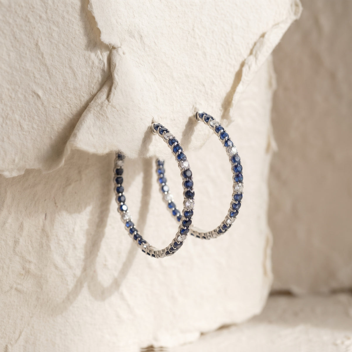 Sapphire and diamond hoops displayed on textured paper