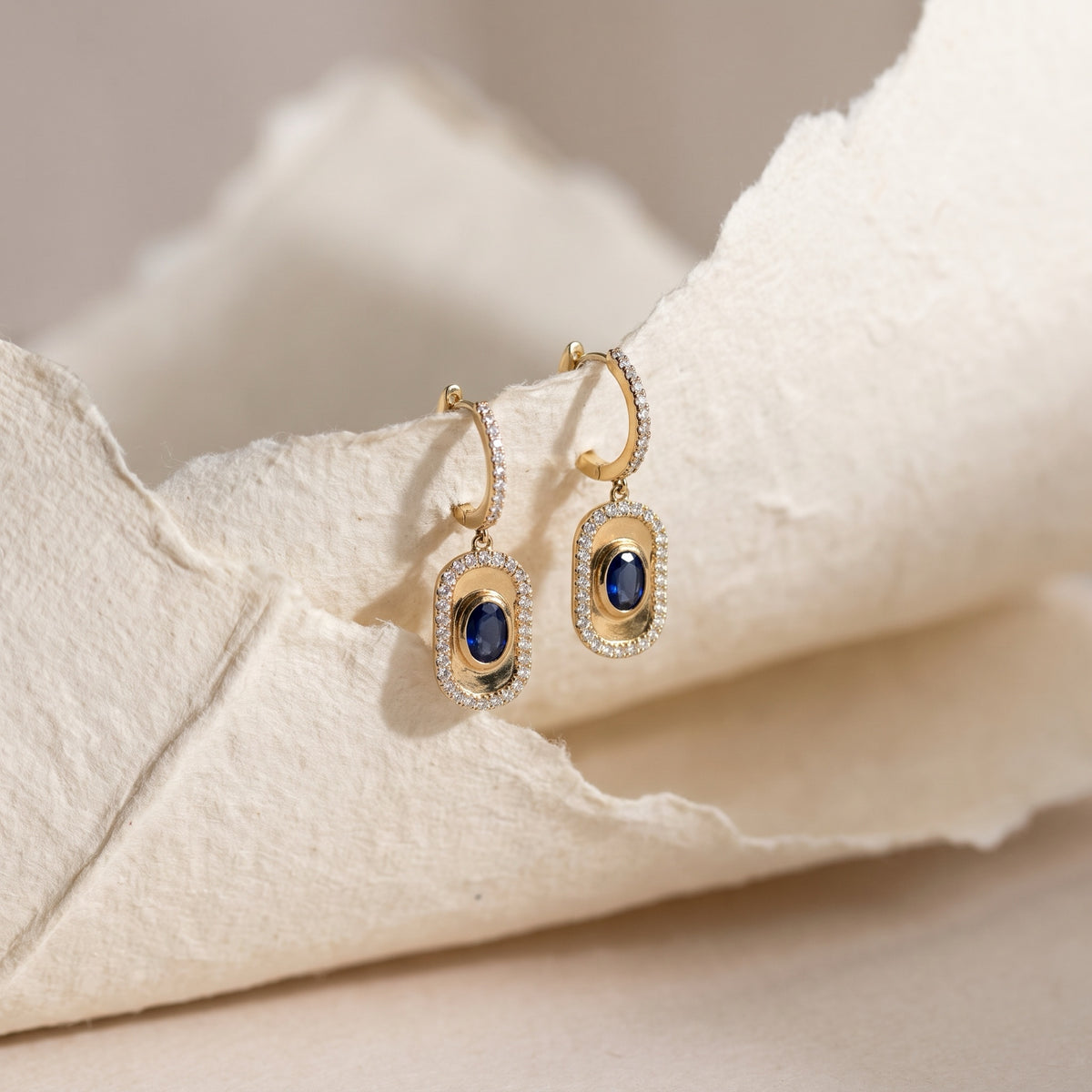 Sapphire halo drop earrings on textured paper